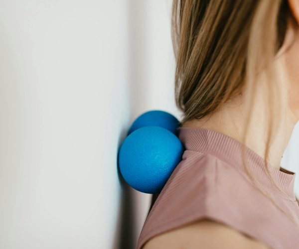 Close-up of woman using blue massage balls for neck relief against a wall.