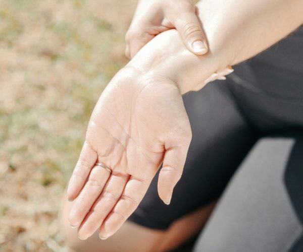 Person gripping wrist in pain, highlighting injury and support outdoors.