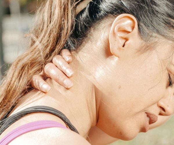Close-up of a woman holding her neck, showing discomfort and pain outdoors.