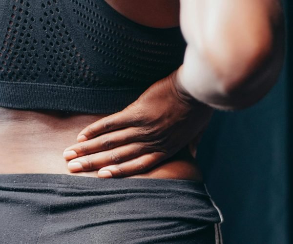 An adult of African descent holding their lower back in pain, indicating discomfort or injury.