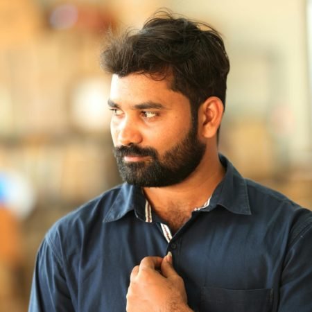 A thoughtful man with a beard and blue shirt posing indoors, displaying a stylish watch.